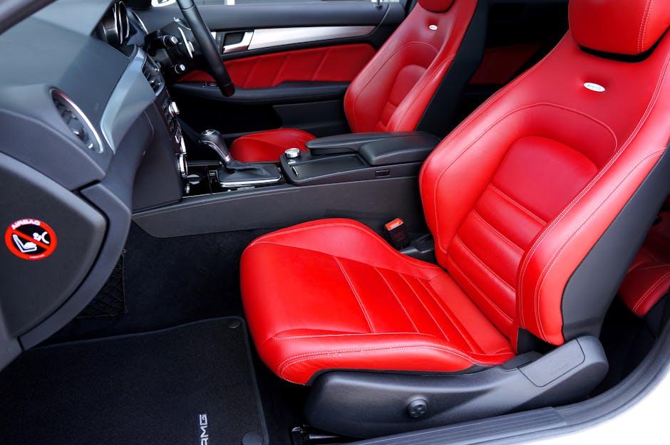 Close-up view of the front interior of a car with black and red leather seats. The seats are clean, glossy, and free of dust or stains, highlighting the smooth and well-maintained surface. The center console and gear shift are visible, with minimal clutter. The surrounding dashboard is dark with metallic accents, and the floor mat appears clean. The lighting inside the vehicle is natural, illuminating the shiny leather and clear surfaces, reflecting professional cleaning and surface care. This image exemplifies the meticulous interior surface cleaning and maintenance that Carpet Cleaners Knightsbridge offers as part of their domestic cleaning and deep cleaning services, especially in vehicle upholstery care on Brompton Road. The setting emphasizes hygiene, surface shine, and care for both car interiors and home furniture surfaces, aligning with upholstery cleaning and stain care expertise.