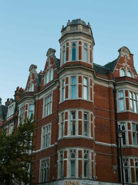 Exterior view of a historic multi-story building with ornate architectural details and large illuminated signs displaying the word 'SHOPS' on one side. The building features tall windows and decorativ